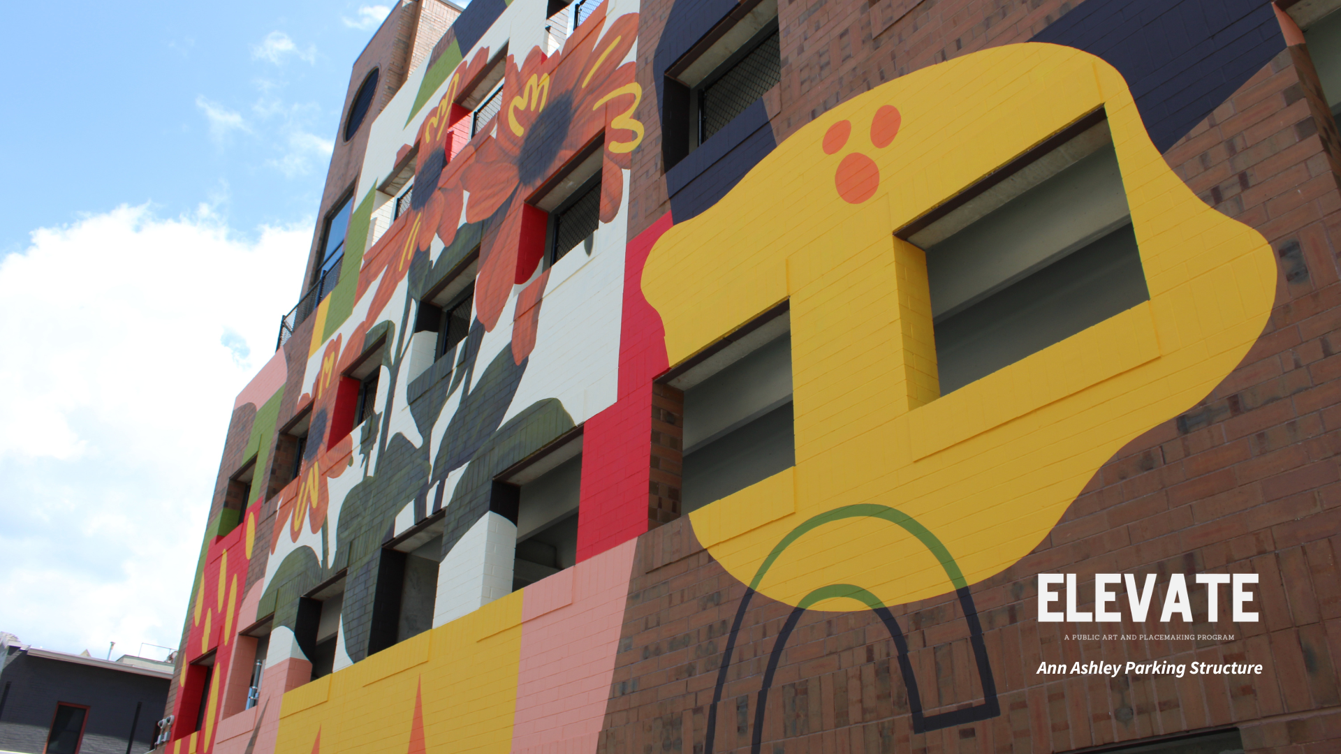 a colorful painted mural consisting of fruits, flowers, and abstract shapes on the surface of a parking structure.